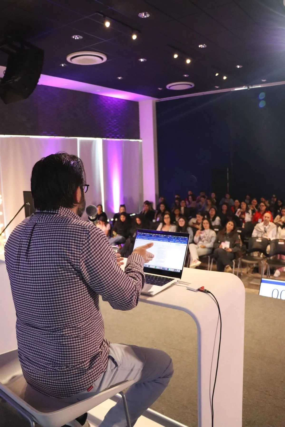 Héctor Sauza de espaldas en el escenario, hablando frente a un auditorio lleno