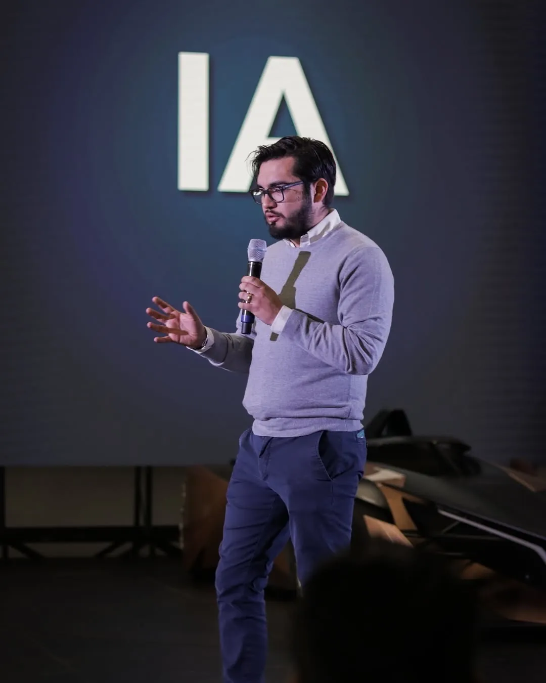 Héctor Sauza con micrófono frente a una pantalla con las letras IA