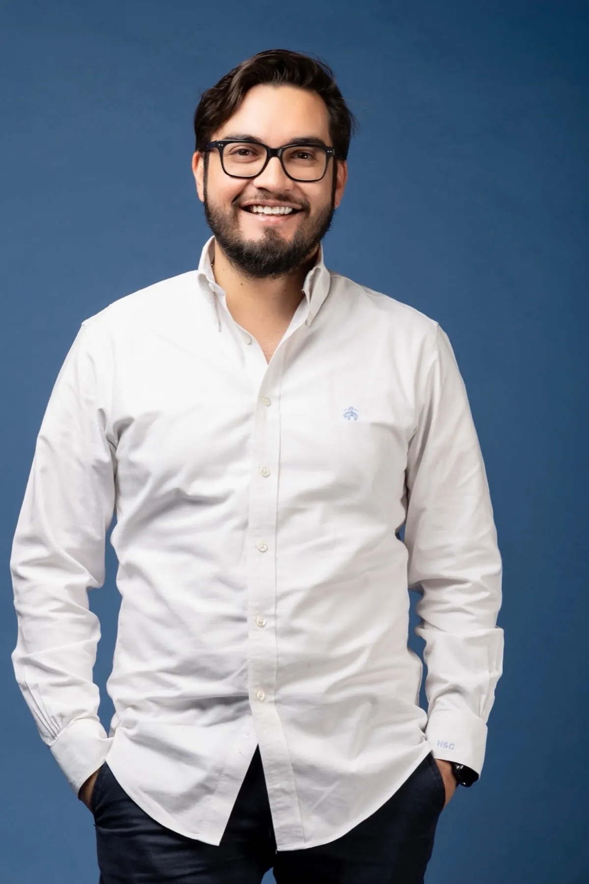 Héctor Sauza sonriendo, con camisa blanca, sobre fondo azul